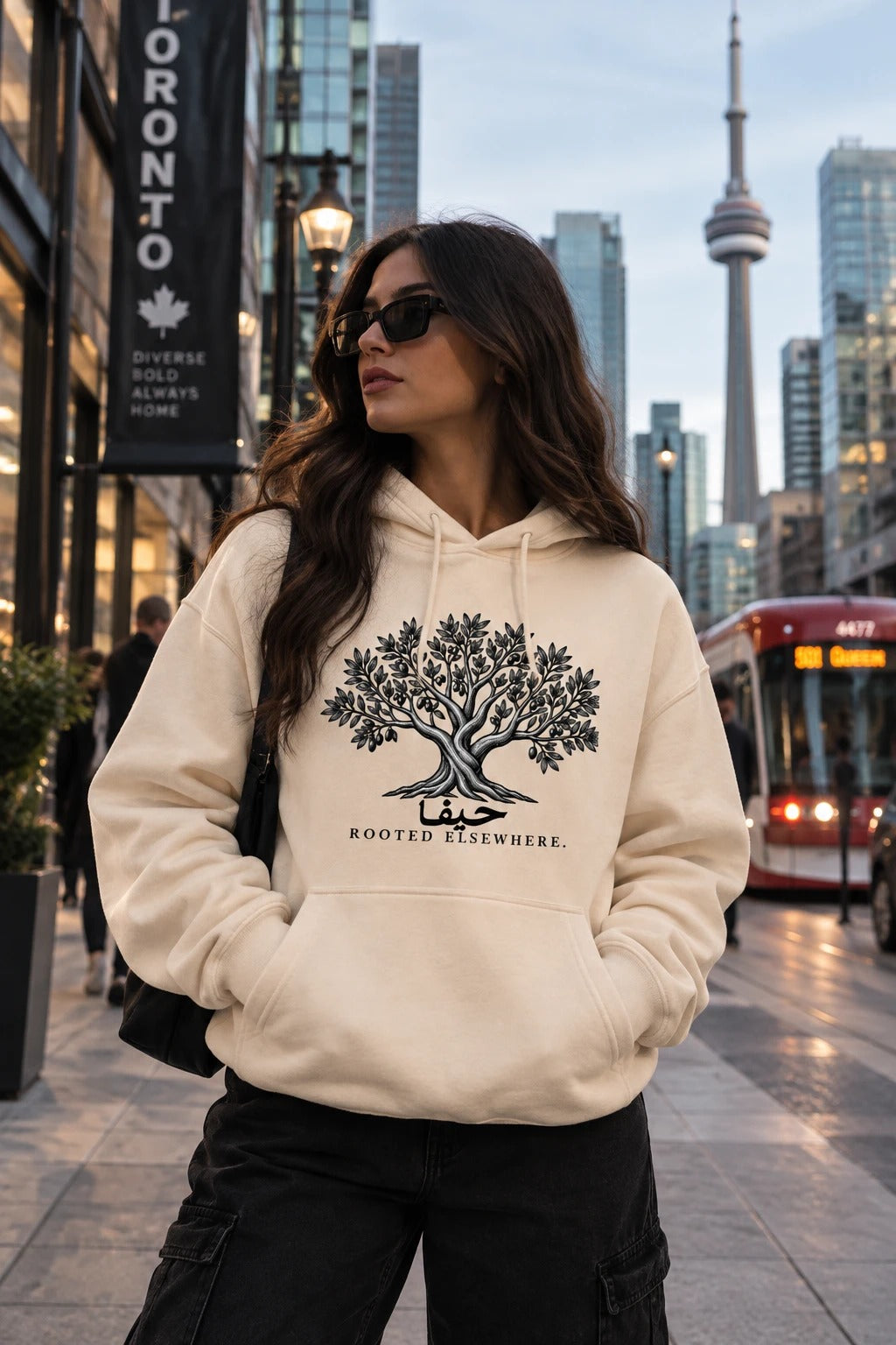 The Roots — Judhour cream hoodie with olive tree and Rooted Elsewhere, Toronto street
